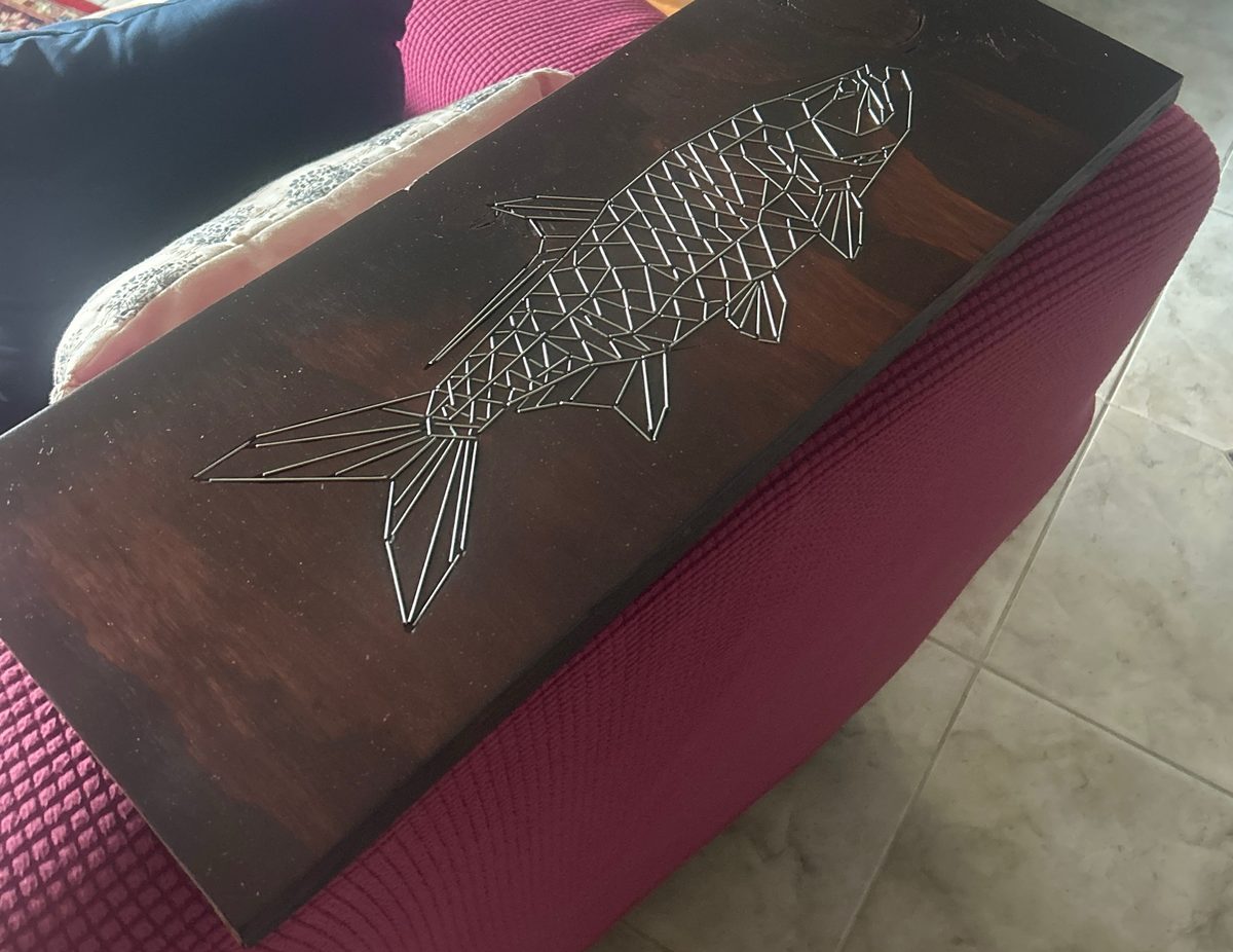 Dark stained wood panel with a fish rendered in wire linework